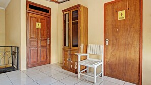 A hallway with three wooden doors, each marked with a gender sign, and a white chair in the center. - OYO 92851 Homestay Borobudur Specpacker Syariah (Borobudur)