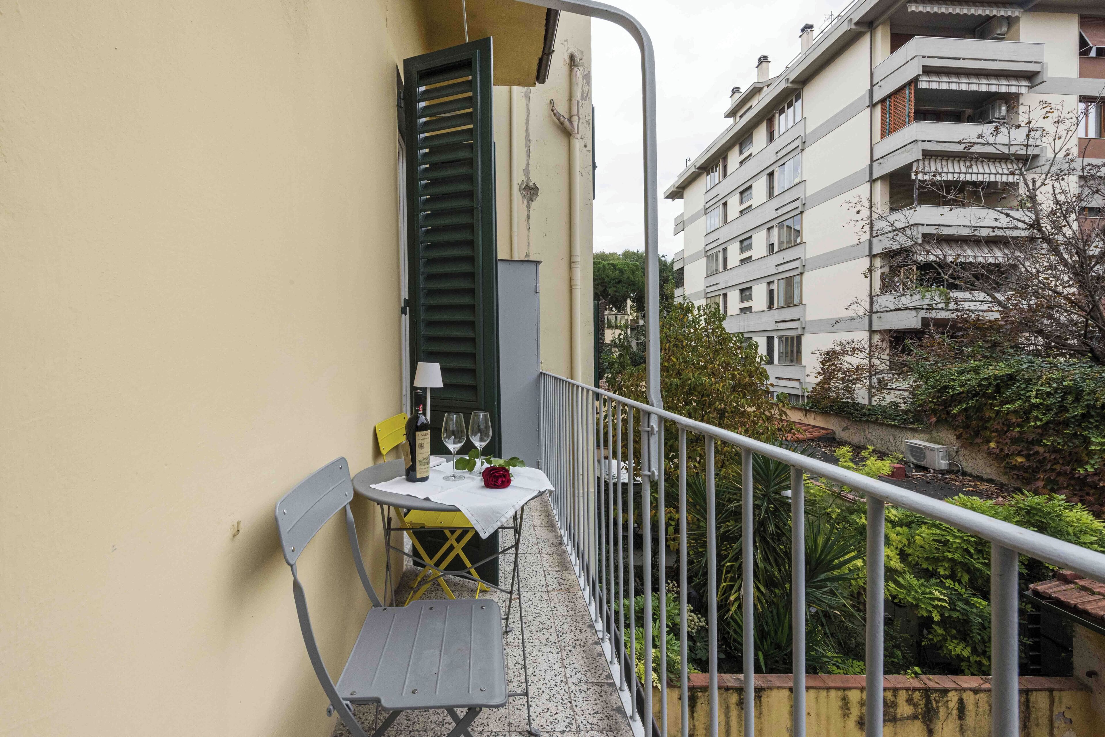 A balcony with a table, two chairs, a bottle, and two wine glasses.