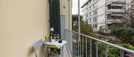 A balcony with a table, two chairs, a bottle, and two wine glasses.