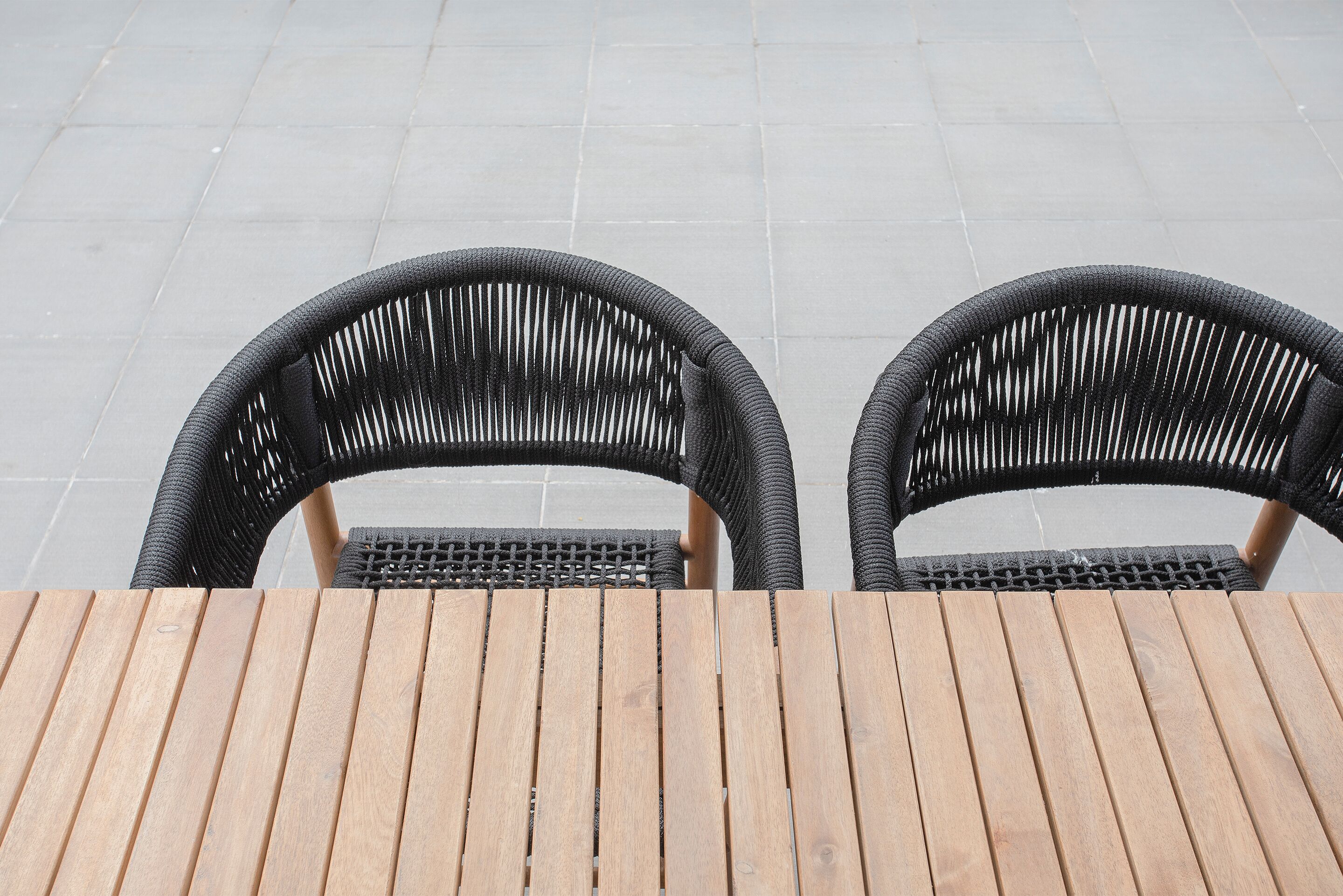 Zwei Korbstühle und ein Holztisch auf einer gefliesten Terrasse.