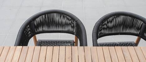 Duas cadeiras de vime e uma mesa de madeira num pátio com ladrilhos.