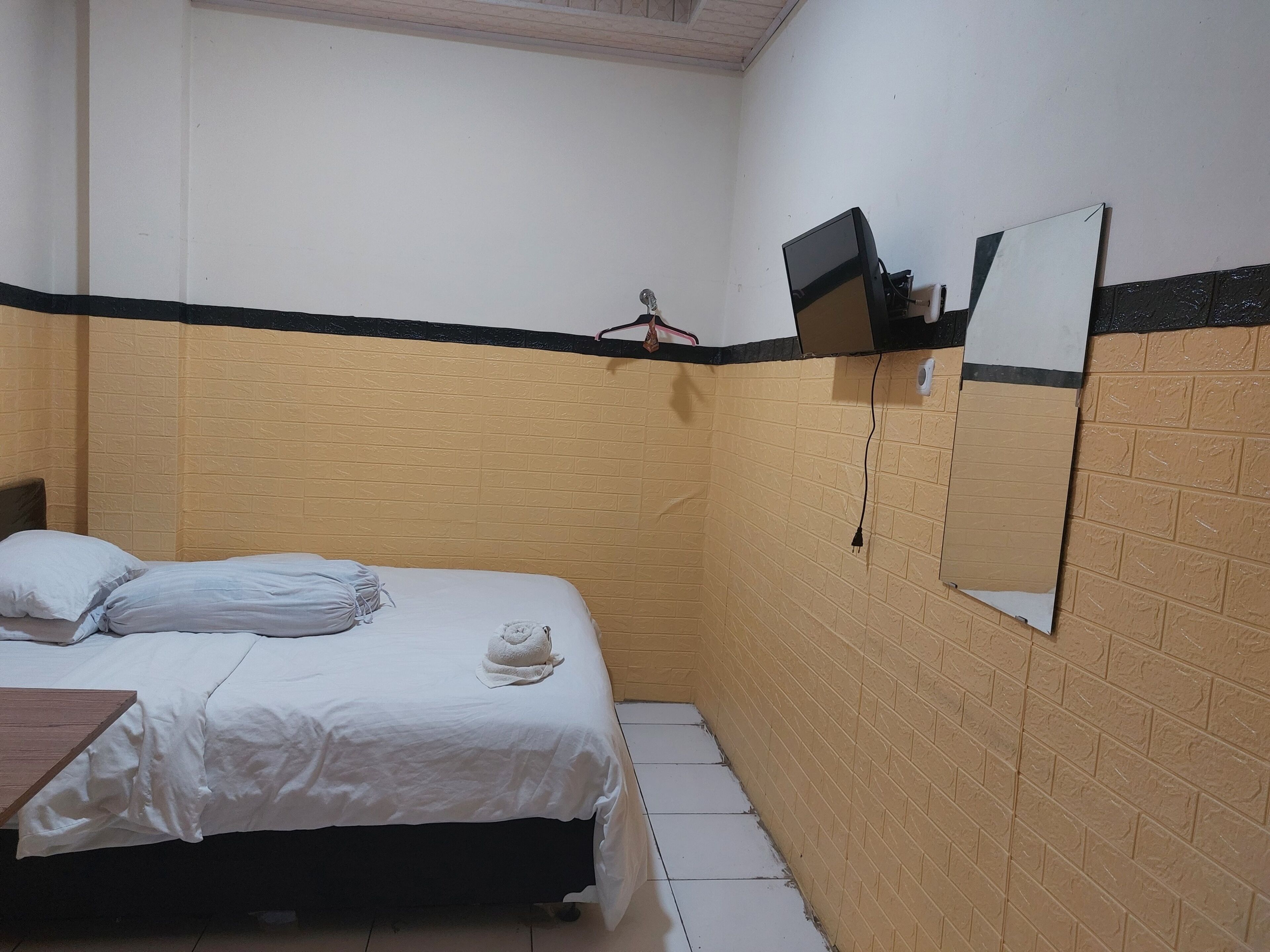 Una habitación pequeña con una cama individual, un edredón blanco sencillo, una toalla y una mesita de noche de madera.