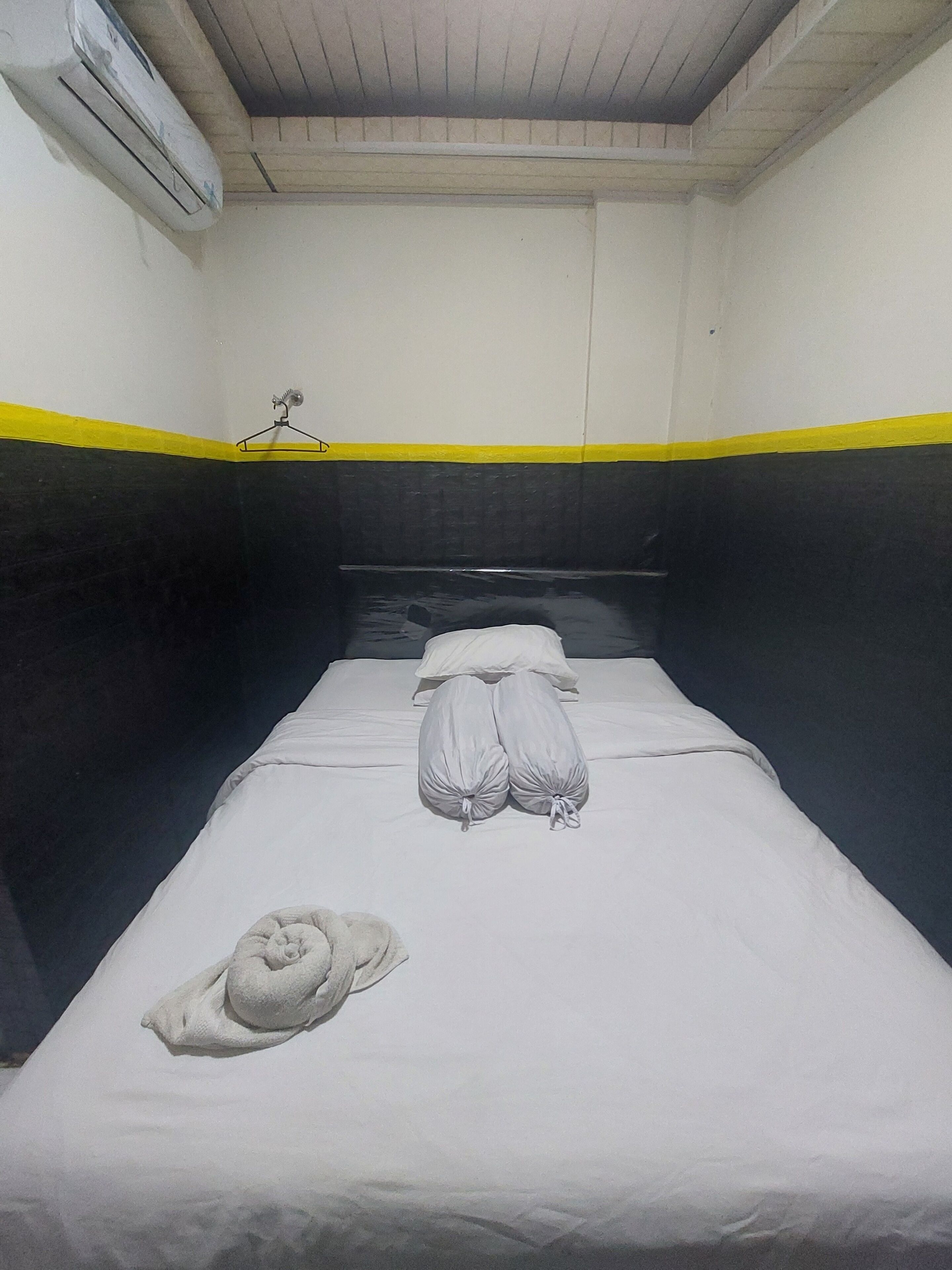 A single bed with a white mattress, two pillows, and a folded towel.