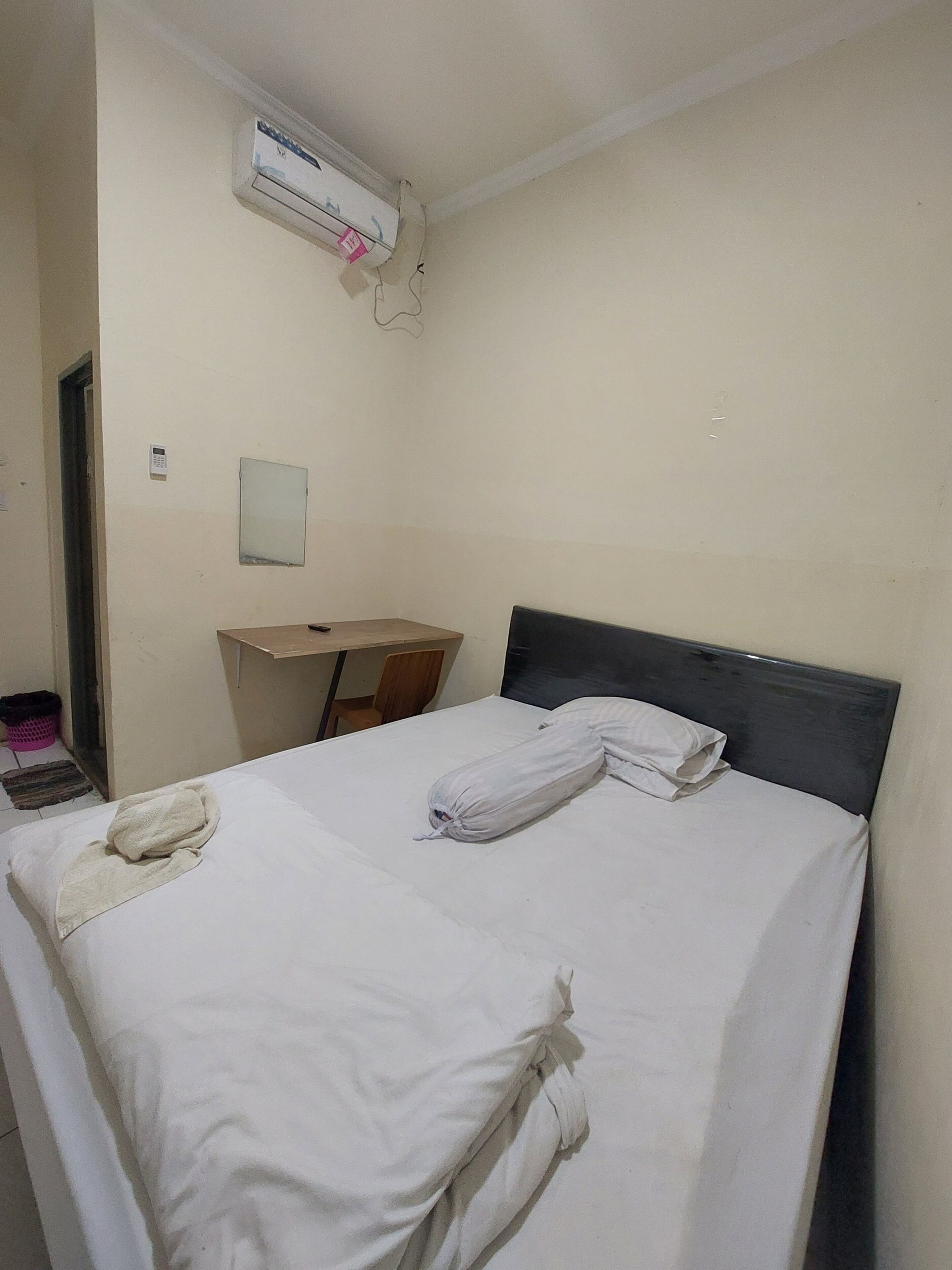 A hotel room with a bed, a desk, and an air conditioning unit.