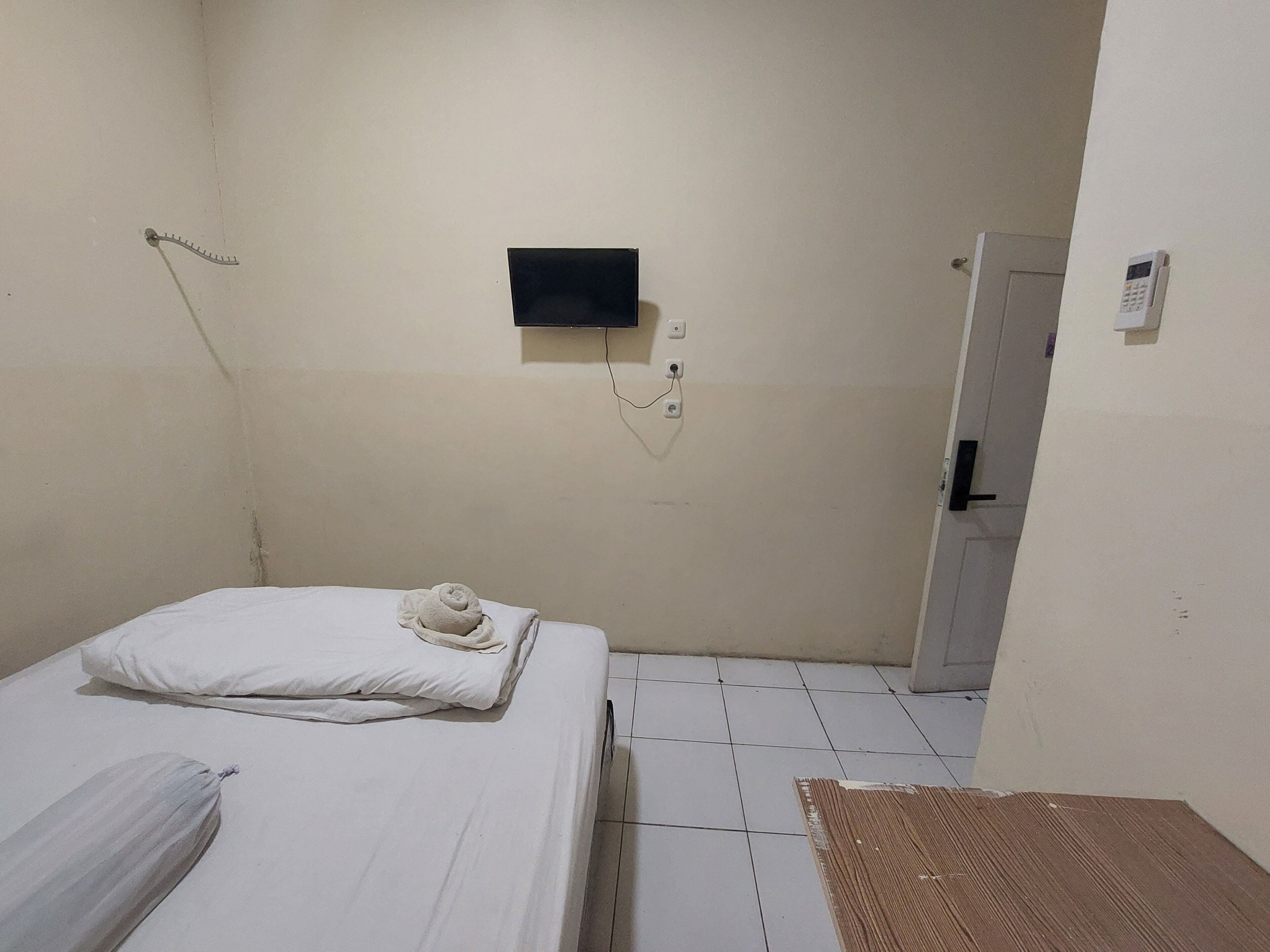 A small, sparsely furnished room with a bed, a small TV mounted on the wall, and a door leading to another room.