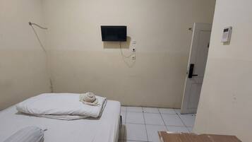 A small, sparsely furnished room with a bed, a small TV mounted on the wall, and a door leading to another room.