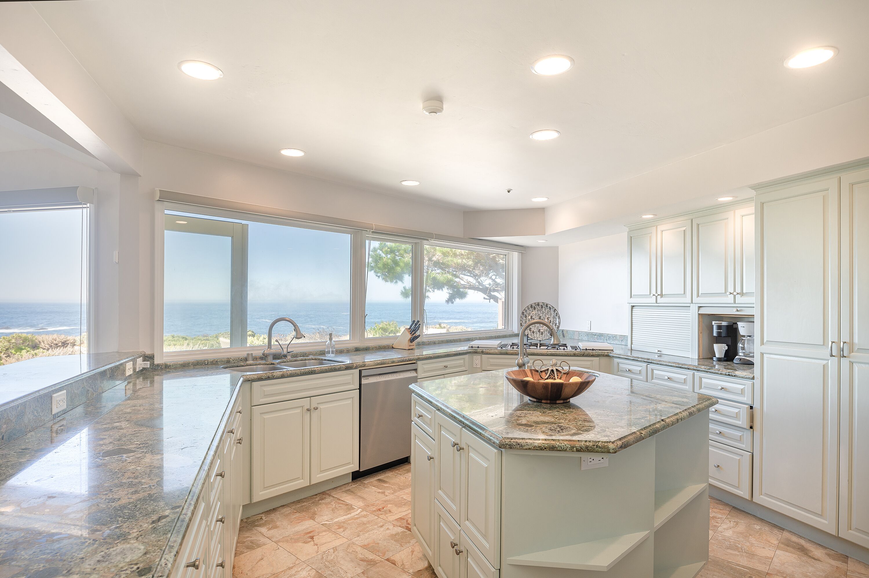 A modern kitchen with a large island, white cabinetry, and a view of the ocean.