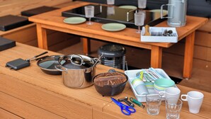 A wooden table with various kitchen items including a pot, pan, and utensils, a small grill, and a tray of dishes. - piilo asobi&stay (Yamanakako)