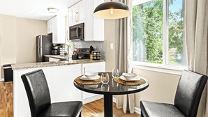 A modern kitchen with white cabinets, a black refrigerator, and a dining area with a round table and black chairs. - New! Comfortable 1BR Upper Flat, Roseville Downtown (Roseville)