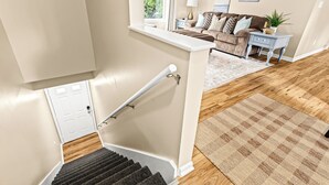 A staircase leading to a living room with a sofa, a side table, and a window with a view of greenery. - New! Comfortable 1BR Upper Flat, Roseville Downtown (Roseville)