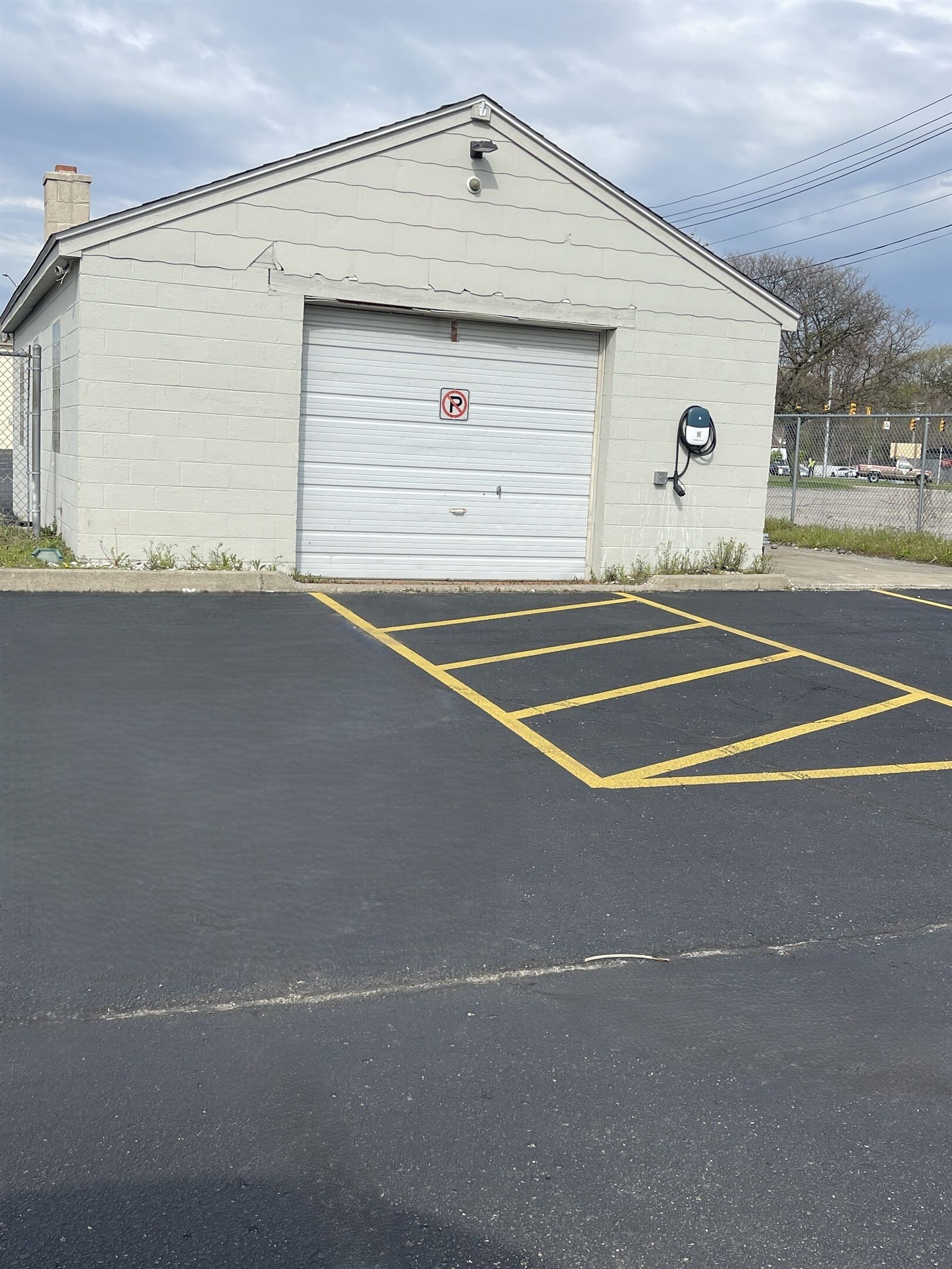 A building with a garage door, a no parking sign, and a parking space marked with yellow lines.