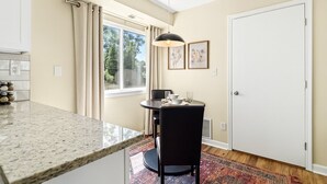 A modern kitchen with a granite countertop, a dining area with a round table and chairs, and a large window with curtains. - Spacious 1BR End Unit, Heart of Roseville (Roseville)