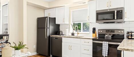 A modern kitchen with white cabinets, a black refrigerator, a microwave, and a stove.