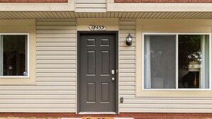 A residential house with a dark gray front door, beige siding, and a 'hello' mat at the entrance. - Spacious 1BR End Unit, Heart of Roseville (Roseville)
