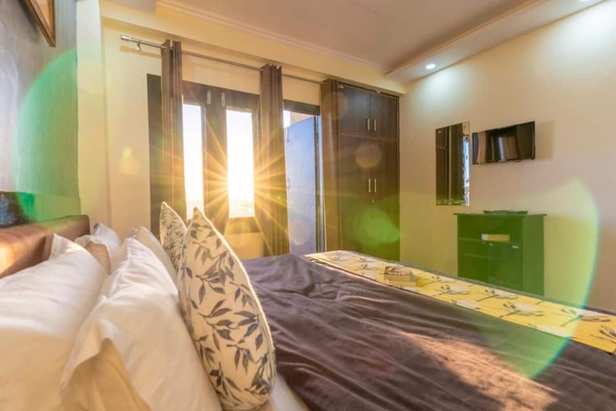 Une chambre d’hôtel avec un lit, une armoire, un meuble vert et un téléviseur fixé au mur.
