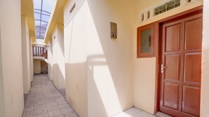 A narrow corridor with tiled flooring, a wooden door, and a window on the right wall. - Hotel O Sunyoto Homestay Syariah (Mojosari)