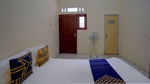 A room with a bed, two pillows, a standing fan, a red door, and a yellow door. - Hotel O Sunyoto Homestay Syariah (Mojosari)