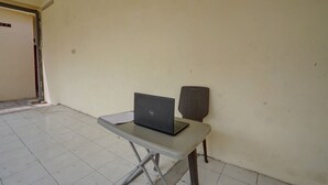 A room with a laptop on a table, a wicker chair, and a tiled floor. - Hotel O Sunyoto Homestay Syariah (Mojosari)