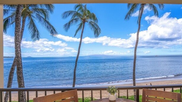 Une table avec des assiettes et des verres sur un balcon donnant sur une plage bordée de palmiers et sur l’océan.