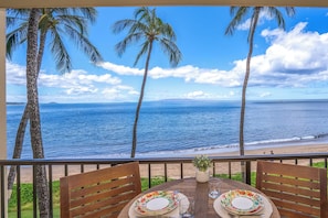 A table with plates and glasses on a balcony overlooking a beach with palm trees and the ocean. - Beachfront Kihei condo w/ ocean views and hot tub (Kihei)