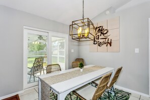 A dining area with a white table, wicker chairs, a hanging light fixture, and a sliding glass door leading to an outdoor patio. - 15 mins from Perdido beach,  Lakefront with Firepit, near NAS/Blue Angels (Pensacola)