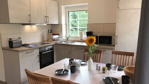 Una cocina moderna con comedor, que cuenta con una isla central, sillas de madera y un ventanal con vistas a la vegetación.