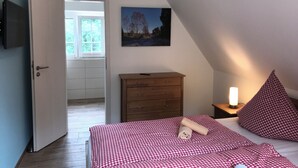 Un dormitorio con colcha a cuadros, cómoda de madera, pintura en la pared y puerta que da a otra habitación.