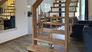 Un interior moderno con una escalera de madera, una zona de comedor y un salón con un ventanal grande.