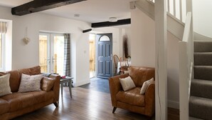 A spacious living room with two leather sofas, a dining area with a table and chairs, and a staircase leading to an upper floor. - The Milking Parlour - Luxury Cottages (Malmesbury)