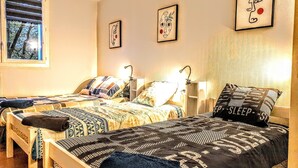 A room with two beds, each with patterned bedding and pillows, a window with blinds, and wall-mounted artwork.