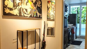 A hallway with a tiled floor, a standing heater, a vacuum cleaner, and two large abstract paintings on the wall.
