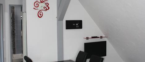 A modern, minimalist room with a black dining table and chairs, a white wall with a red decorative element, and a ceiling with recessed lighting.