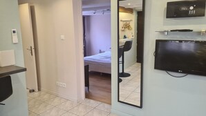 A hotel room with a bed, a TV, a mirror, and a door leading to another room. - Riesling, Gites des Dix Vins (Dangolsheim)