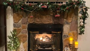 Een haard met een stenen bovenplaat, een kerstboom en een brandende kaars.