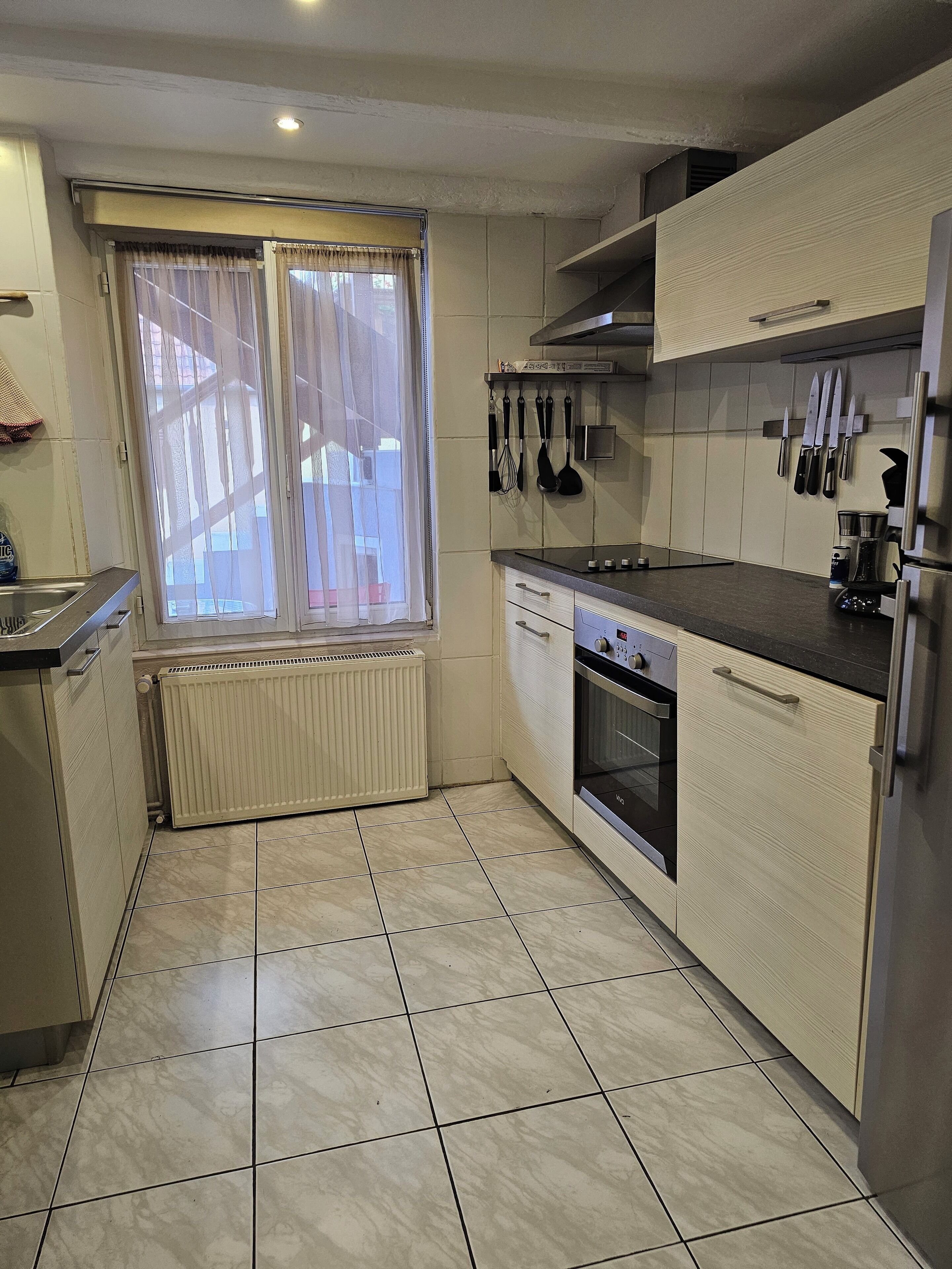 A kitchen with white cabinets, a stove, oven, and a window with curtains.