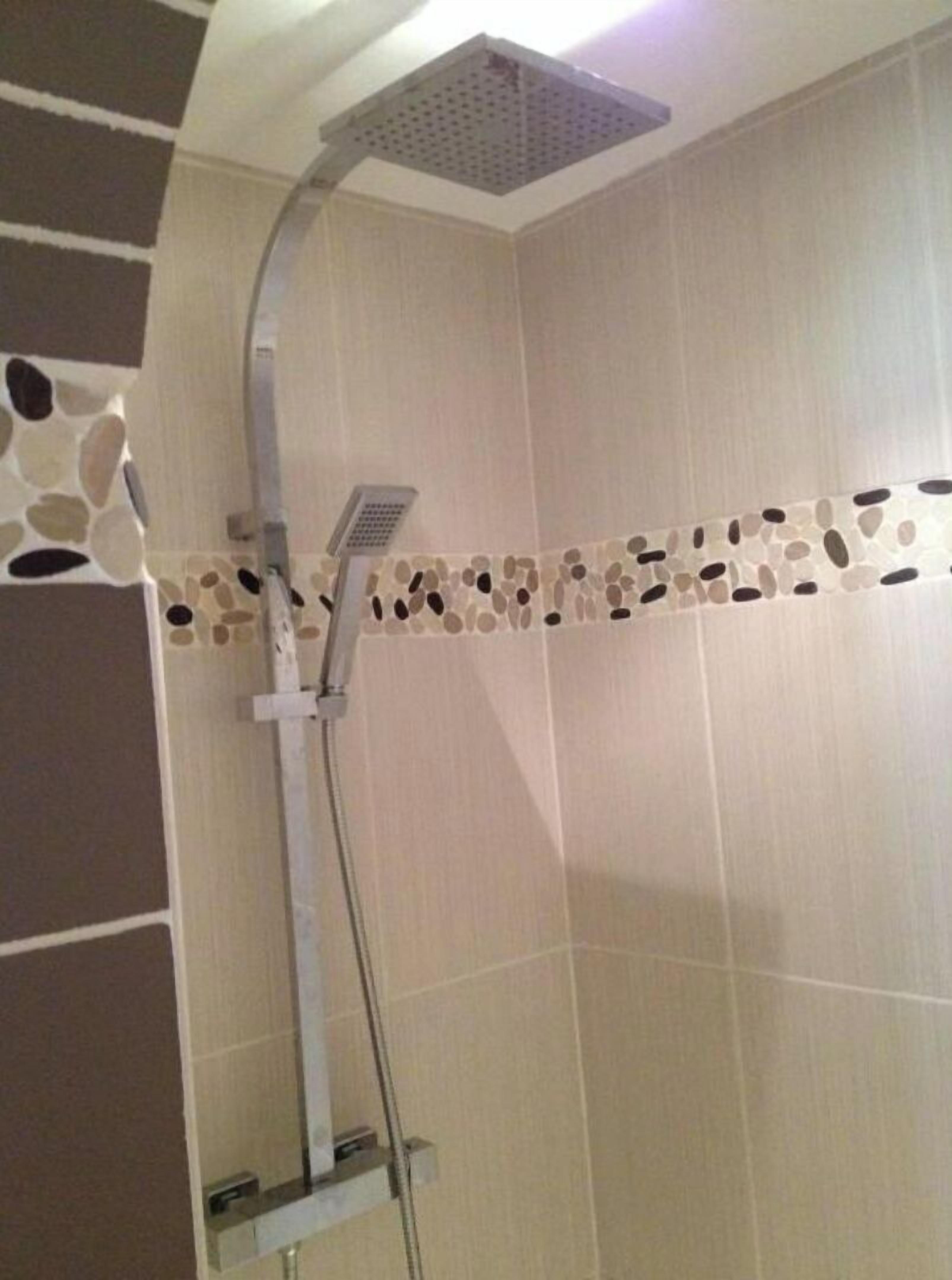 A shower with a square ceiling head and a wall-mounted control panel.