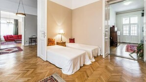 Une chambre avec deux lits simples, une table de chevet avec une lampe, un canapé rouge et un parquet en bois à motifs chevrons.