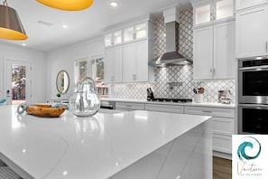 A modern kitchen with white cabinetry, a large island, and stainless steel appliances. - Ash in the Sand - Private Pool / Golf Cart / 6 Bikes / Game Room (Santa Rosa Beach)