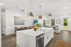 A modern kitchen with a central island, pendant lighting, and a view of the outdoors. - Ash in the Sand | 30A | Privte Pool | Golf Cart | Bikes | Games (Santa Rosa Beach)