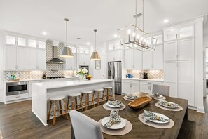 A modern kitchen with white cabinetry, a central island with bar stools, stainless steel appliances, and pendant lighting. - Ash in the Sand | 30A | Privte Pool | Golf Cart | Bikes | Games (Santa Rosa Beach)