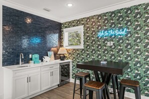 A modern kitchen with a black tiled backsplash, a white countertop, and a neon sign. - Ash in the Sand | 30A | Privte Pool | Golf Cart | Bikes | Games (Santa Rosa Beach)