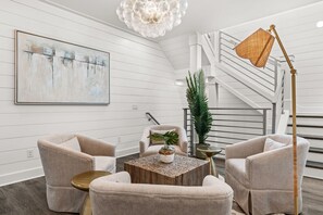 A modern living room with a staircase, a chandelier, and a large abstract painting. - Ash in the Sand | 30A | Privte Pool | Golf Cart | Bikes | Games (Santa Rosa Beach)
