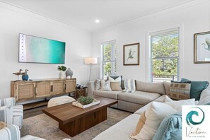 A modern living room with a neutral color palette, featuring a sofa set, a wooden coffee table, and a large abstract painting. - Ash in the Sand - Private Pool / Golf Cart / 6 Bikes / Game Room (Santa Rosa Beach)