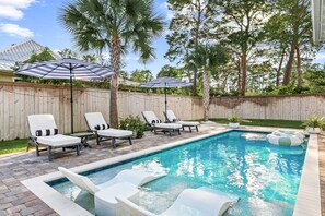 A backyard with a swimming pool, lounge chairs, and umbrellas. - Ash in the Sand | 30A | Privte Pool | Golf Cart | Bikes | Games (Santa Rosa Beach)