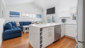 Et moderne køkken med hvide skabe, en indbygget ø og et spiseområde med en blå sofa.