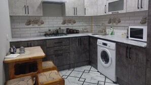 Una cucina compatta con mobili grigi, forno integrato, microonde, lavatrice e un piccolo tavolo in legno con sgabelli.