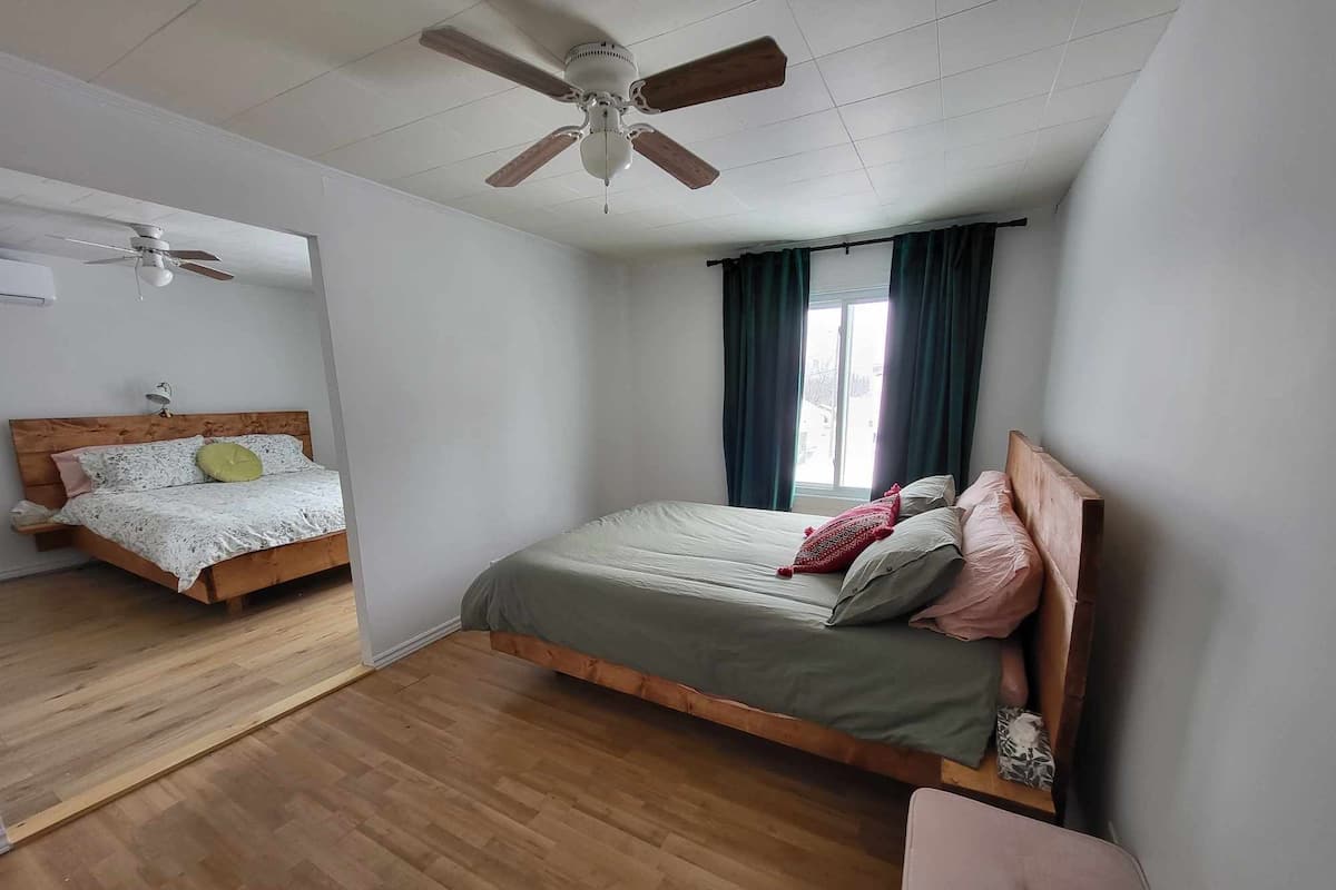 A bedroom with a wooden bed, a ceiling fan, and a window with curtains.