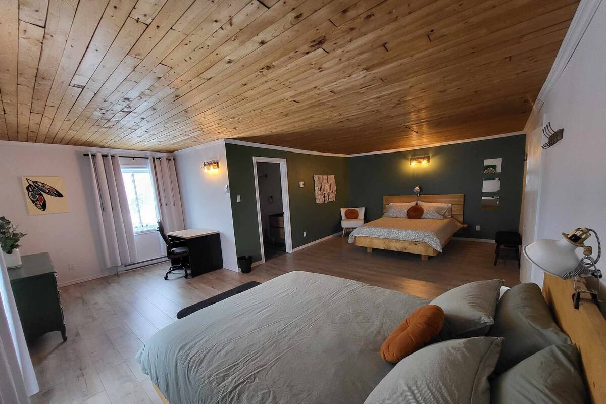 A bedroom with a wooden ceiling, a large bed, a desk, and a chair.