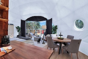 Un interior estilo iglú con una mesa de comedor de madera, sillas y vistas a través de un ventanal grande.