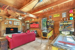 A cozy room with a red sofa, wooden walls, a ceiling fan, a TV, and various arcade games.